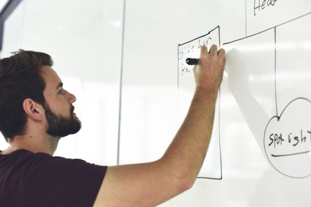 An apprentice draws on a white board