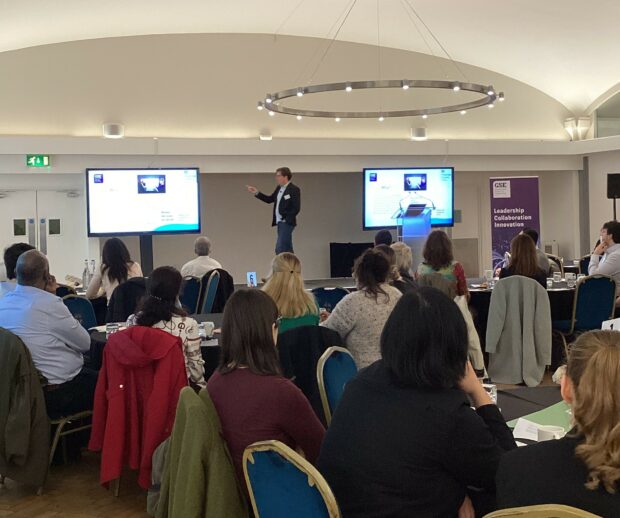 Ben Buchanan presents to a room of attendees at the Leadership Values masterclass. The attendees are seated on round tables facing the stage.